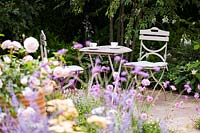 Seating area in cottage garden surrounded by soft, pastel summer flowers. Best of Both Worlds garden, Sponsored by BALI, RHS Hampton Court Palace Flower Show, 2018.
