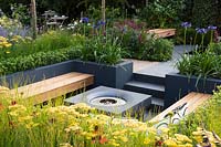 Modern seating area with fireplace surrounded by raised flower beds with 
Achillea, Agapanthus 'Navy Blue' - syn. 'Midnight Star', and Buxus sempervirens.
 Best of Both Worlds garden 
RHS Hampton Court Palace Flower Show 2018