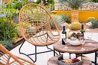 Seating area with wooden table set with glasses, wines and fruits in the garden.
 Santa Rita 'Living La Vida 120' Garden. 
 RHS Hampton Court Palace Flower Show 2018