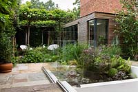 View of paved, modern garden with panelled summerhouse and trained espalier tree arch. 