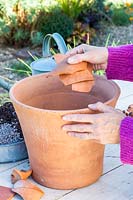 Woman putting broken crocks at the base of terracotta plant pot.