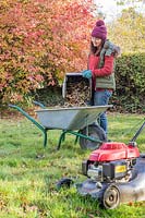 Woman emptying contents of lawn mower grass box into wheelbarrow.