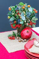 View of completed festive floral arrangement on table, with pomegranate, hazelnuts and crockery.
