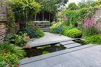View of paved landing pad and narrow pool, across to gravelled area flanked by perennial planting. Garden design by John Davies Landscape.