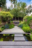 View of paved landing pad and narrow pool, across to gravelled area flanked by perennial planting. Garden design by John Davies Landscape.
