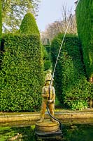 'Fireman' fountain in a pond featuring tall evegreen Yew hedging, 
Plas Brondanw, North Wales, UK. 
