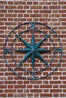 Large metal compass on side of brick wall. 