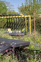 Contemporary, decked seating area under steel-framed pergola, surrounded by mixed naturalistic planting.