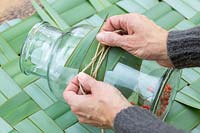 Woman securing Phormium leaf around glass jar with jute string.