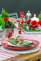 Red, white and green festive table decoration, with potted plants, cut flowers and cermamic reindeer ornaments.