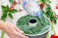 Woman pouring de-ironised water into bundt cake tin full of cut plant material to create frozen floral arrangement.