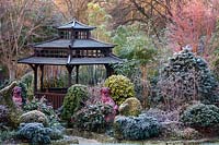 Japanese Tea House-style gazebo in frosted garden, with oriental statuary and shrubs and trees. The Four Seasons Garden, UK.

