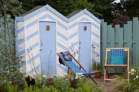 Blue and white beach huts and deck chairs bordered by blue and white coastal planting. Southend Council 'By The Sea' garden at RHS Hampton Court Flower Show, London, 2017. 