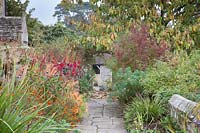 Colourful autumn beds along stone path with Tithonia rotundifolia, Salvia confertiflora, Stipa, Verbena, Euphorbia and Dahlia 'Dovegrove'. Gravetye Manor, Sussex, UK. 