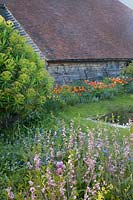 View of old barn in the Sunk Garden with colourful spring planting. Great Dixter Gardens, Sussex, UK.
