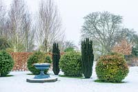 Cast iron urn surrounded by Taxus baccata 'Fastigiata', clipped Viburnum tinus balls and Fagus - beech hedge in snowy garden.