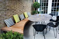 Contemporary garden with white stone patio, with outdoor furniture
 and wooden seating dressed with garden cushions