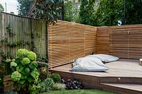 Contemporary garden with cedar battened trellis screen providing privacy
 for stepped decking with and large garden lounge cushions
