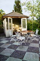 View of summerhouse with paved patio and garden table and chairs. Summerdale Garden, Cumbria, UK. 
