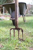 Garden fork in the lawn with wheelbarrow in the background. 