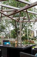 Contemporary patio area in London garden with wood pergola and rafia garden furniture and seating. Designed by Kate Eyre Garden Design. 