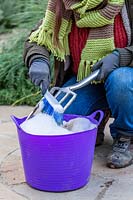 Woman washing metal gardening fork in bucket of soapy water.