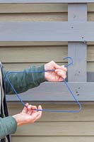 Person pulling coated clothes hanger to shape it into a hook 