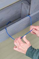 Woman bending coated clothes hanger to shape it into a hook for carrying a hosepipe. 