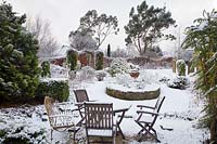 Seating area and raised circular bed in snowy formal garden. 