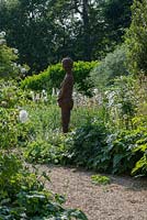 Willow sculpture of figure by Helen Colletta, standing amongst white flowering plants.  