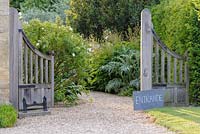 Wooden gates at entrance to garden with roses and Cynara cardunculus - Cardoon. 