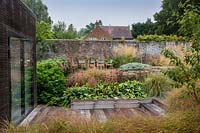 View of wooden decking and surrounding perennial borders in contemporary garden near Winchester, Hants, UK. Designed Elks-Smith Garden Design.