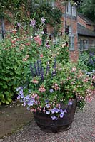 Oak barrel planted with fuchsias, salvias and petunias in the courtyard at Wollerton Old Hall, Market Drayton, UK. 