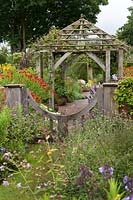 Wooden gateway and pergola surrounded by perennial borders in the Sundial Garden at Wollerton Old Hall Garden, Market Drayton, UK. 