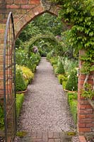 View through brick arch and gateway to Buxus - Box edged borders of the Long Border at Wollerton Old Hall, Shropshire, UK. 