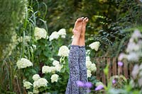 A person practices the position Sarvangasana - shoulder stand in garden.  