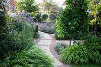 Contemporary English suburban garden with perennial borders and curving geometrically layed brick and natural stone path. Wiltshire, UK. Summer, July.