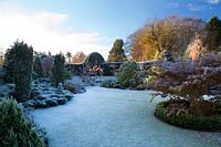 Large, curved and circular beds of shrubs and trees such as Juniperus communis
 Hibernica and  Zelkova serrata 'Kiwi Sunset' set off by frosted lawn, formal hedge in background