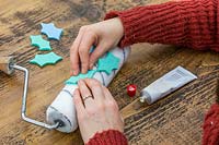 Woman gluing foam holly leaf shapes in a pattern on paint roller.