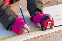 Close up of woman marking piece of wood with tape measure.