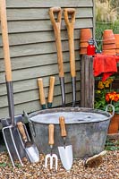 Washing tools: Clean garden tools leaning against side of shed to dry next to metal tub of soapy water.
