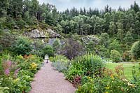 Long, double herbaceous borders and gravel path leading to a boat-shaped arched garden seat. 