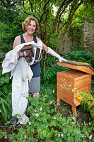 Esther Mendelssohn standing by beehive with beekeepers suit and bee smoker. 