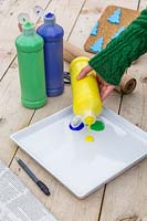 Woman pouring yellow, blue and green paint onto plate for mixing the perfect green.