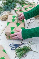 Woman adding pine needle adornment to christmas gift wrapped with hand printed wrapping paper and string.