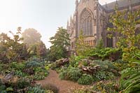 The Stumpery in late summer, with decorative oak stumps, woodland planting and the cathedral beyond. Garden: Arundel Castle, Sussex, UK. 
