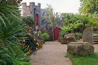 Path alongside large stones, Dicksonia Antarctica - tree fern, Dahlia and 
Canna, to red arched gates in wall 