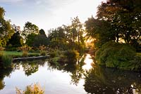 The Lower Pond adjoining the Round Garden is surrounded by trees and shrubs. Llanover Gardens, Monmouthshire, UK.