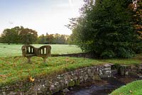 Stone 'Kissing Bench' by stream, with parkland beyond. Llanover Gardens, Monmouthshire, UK. 