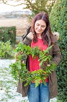 Woman holding up completed moss and fern wreath in snowy garden